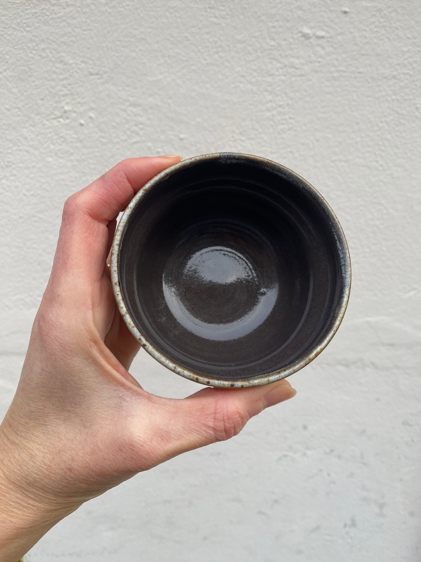 Hand holding a black and beige ceramic cup against a light gray background