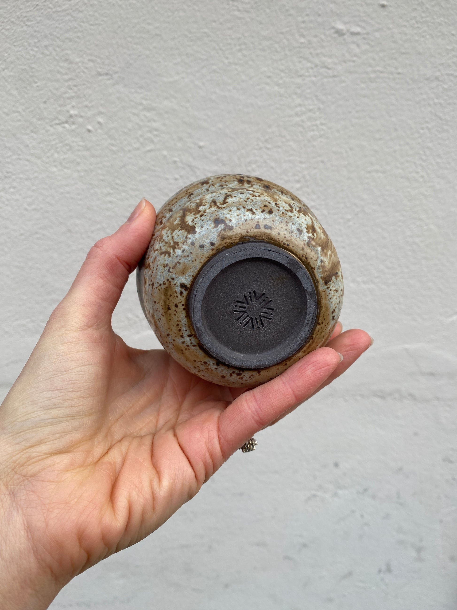 Hand holding a small ceramic pot with a textured surface against a plain background