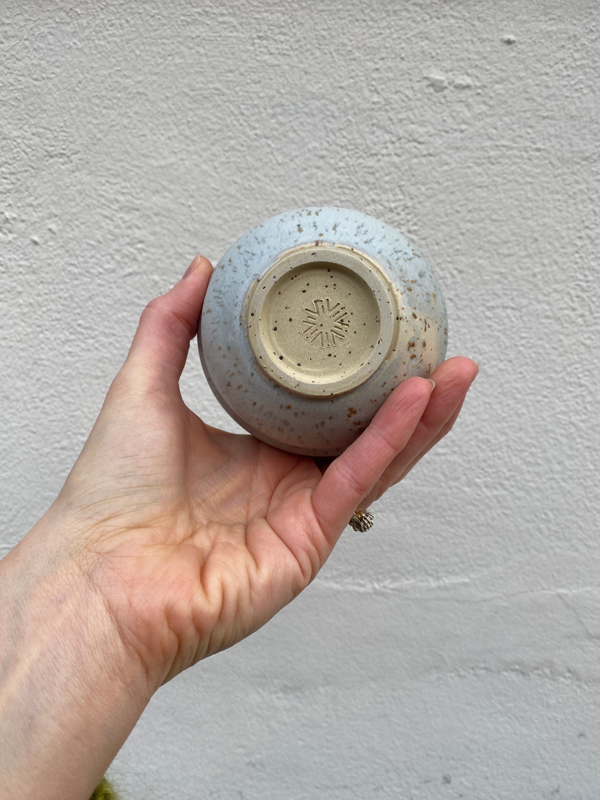 Hand holding a light grey ceramic cup against a plain background
