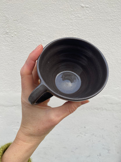 Hand holding a dark ceramic mug against a light background