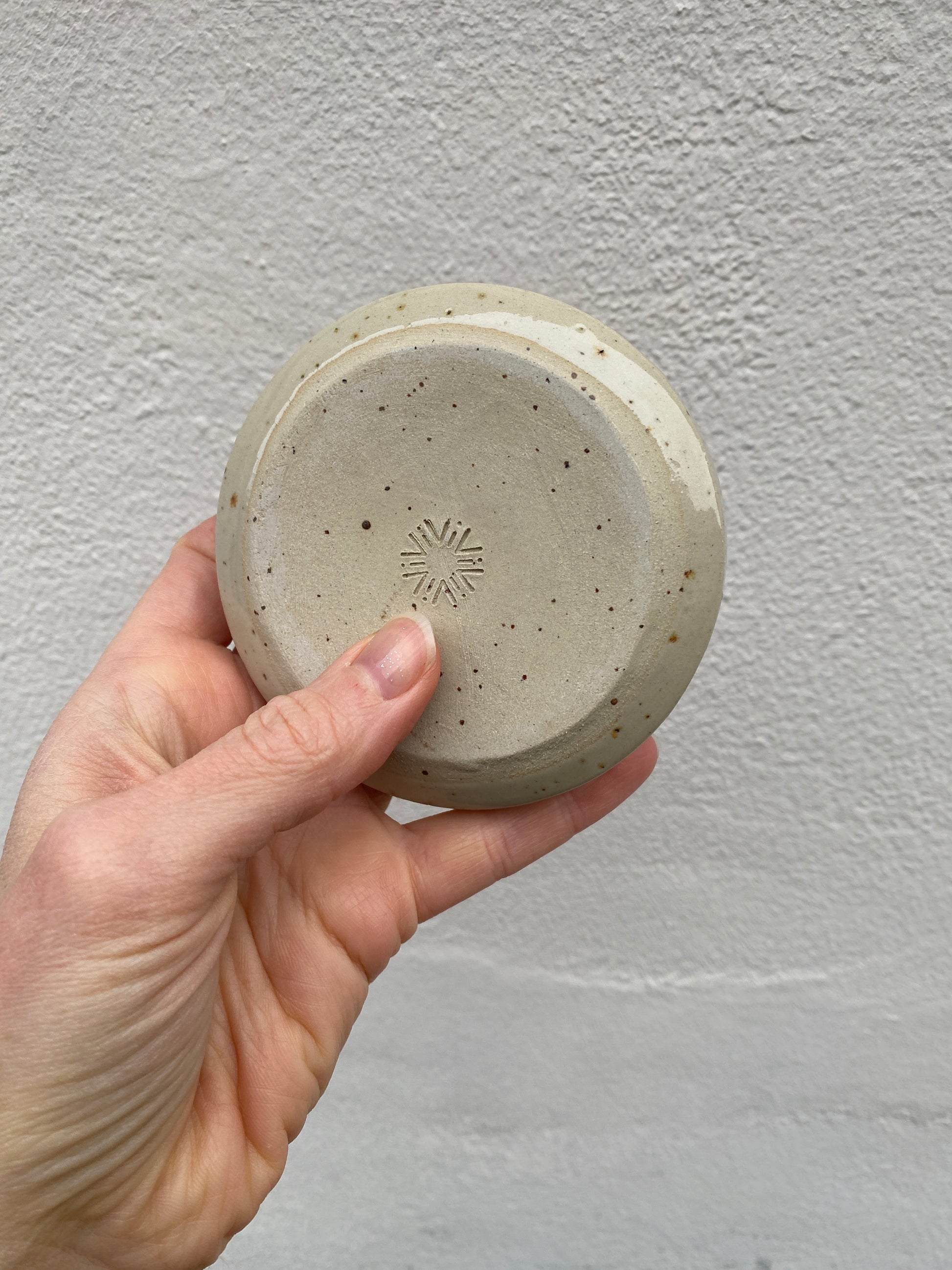 Hand holding a small ceramic candlestick holder showing the backside with a pottery stamp against a plain background