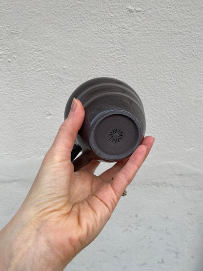 Hand holding a dark gray ceramic cup against a plain background