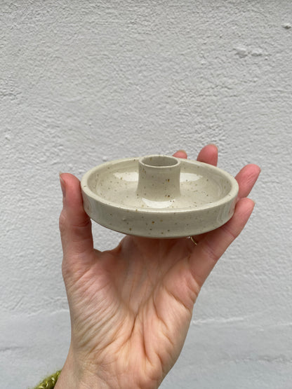 Hand holding a small ceramic candlestick holder against a plain background