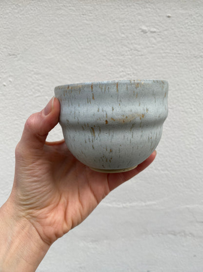 Hand holding a light grey ceramic cup against a plain background