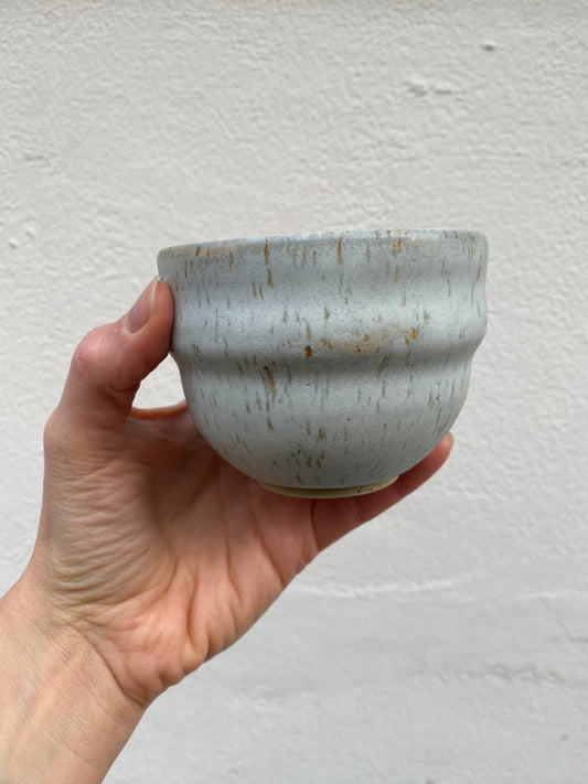Hand holding a light grey ceramic cup against a plain background