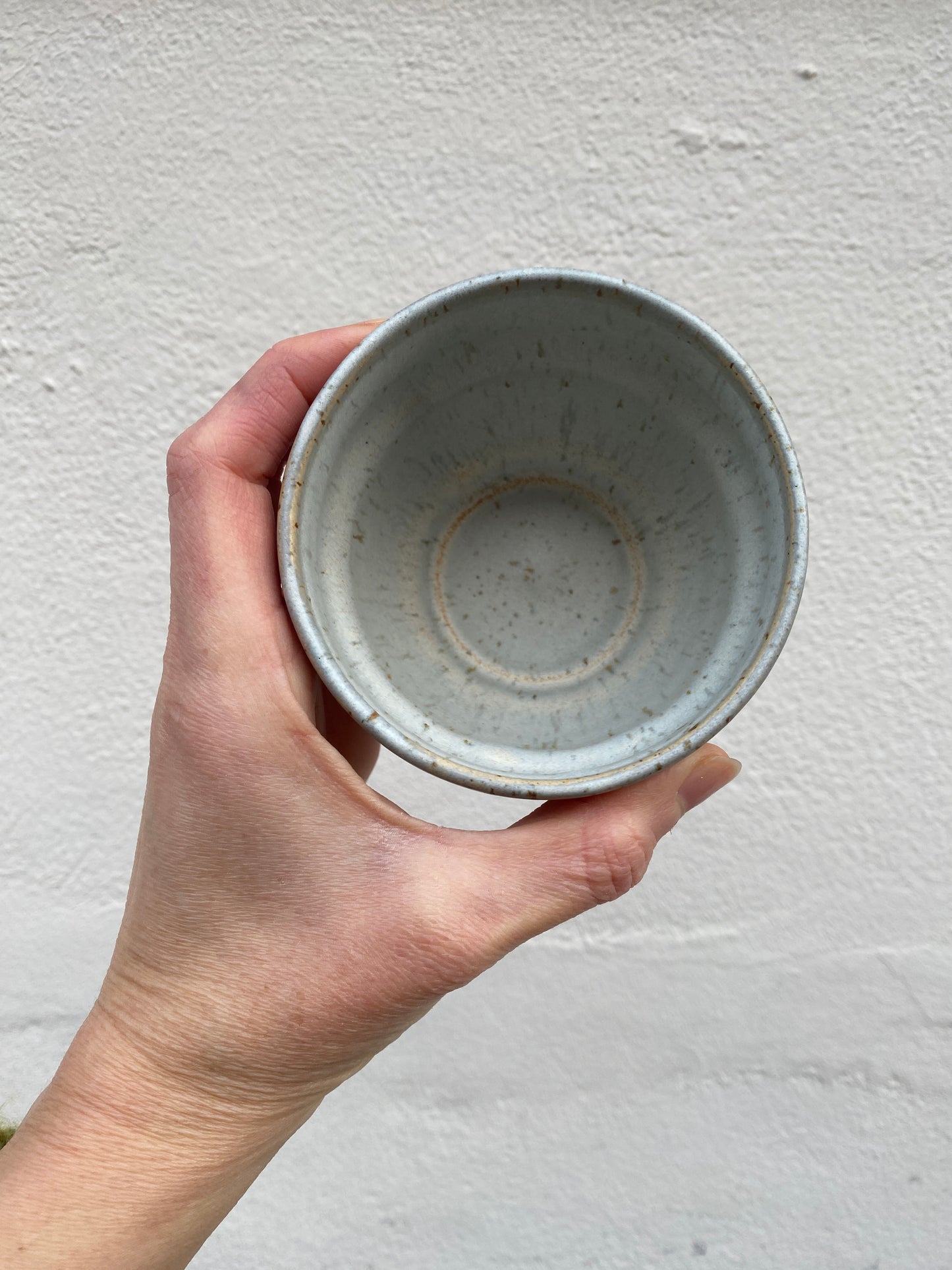 Hand holding a light grey ceramic cup against a plain background
