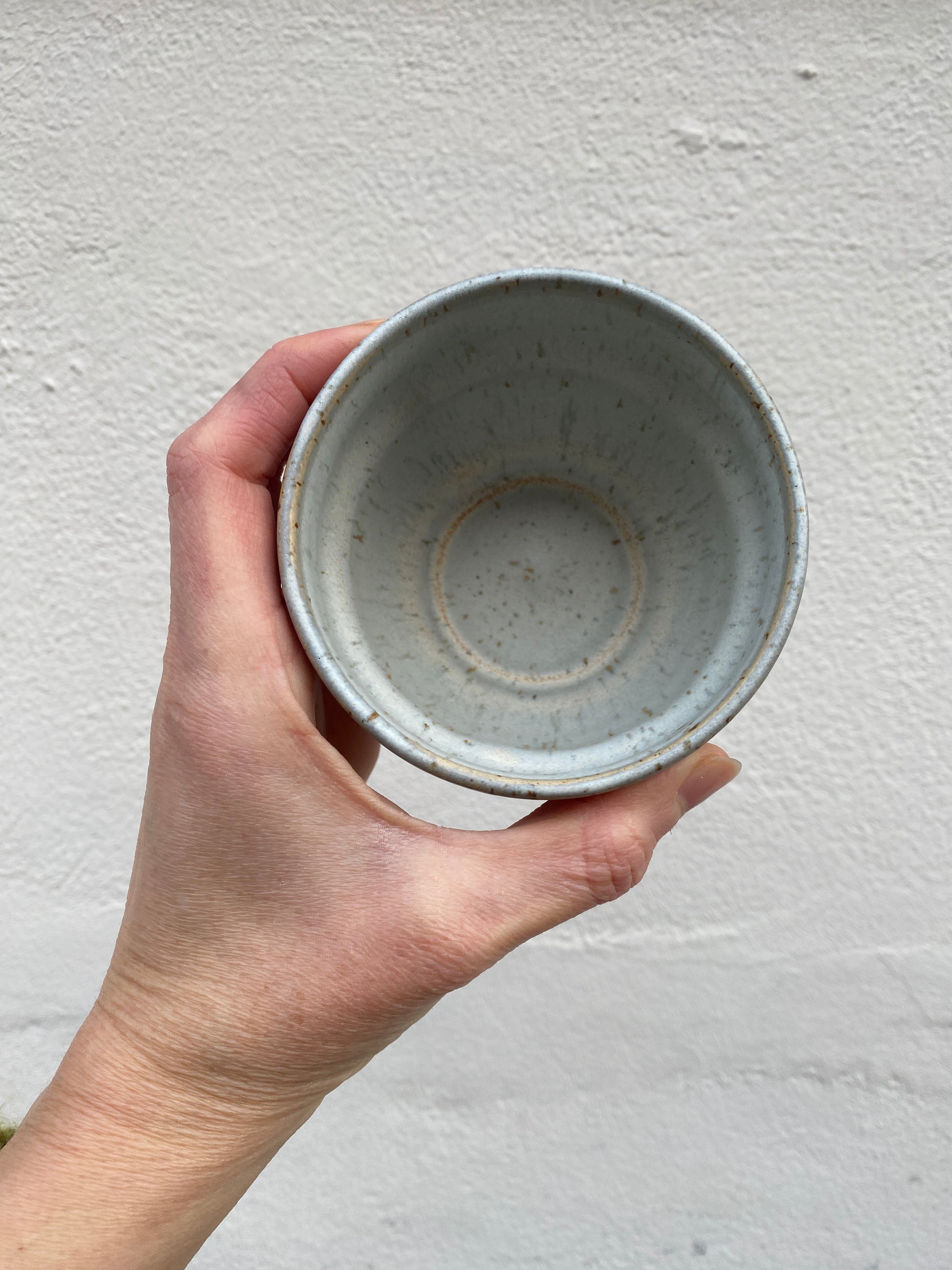 Hand holding a light grey ceramic cup against a plain background