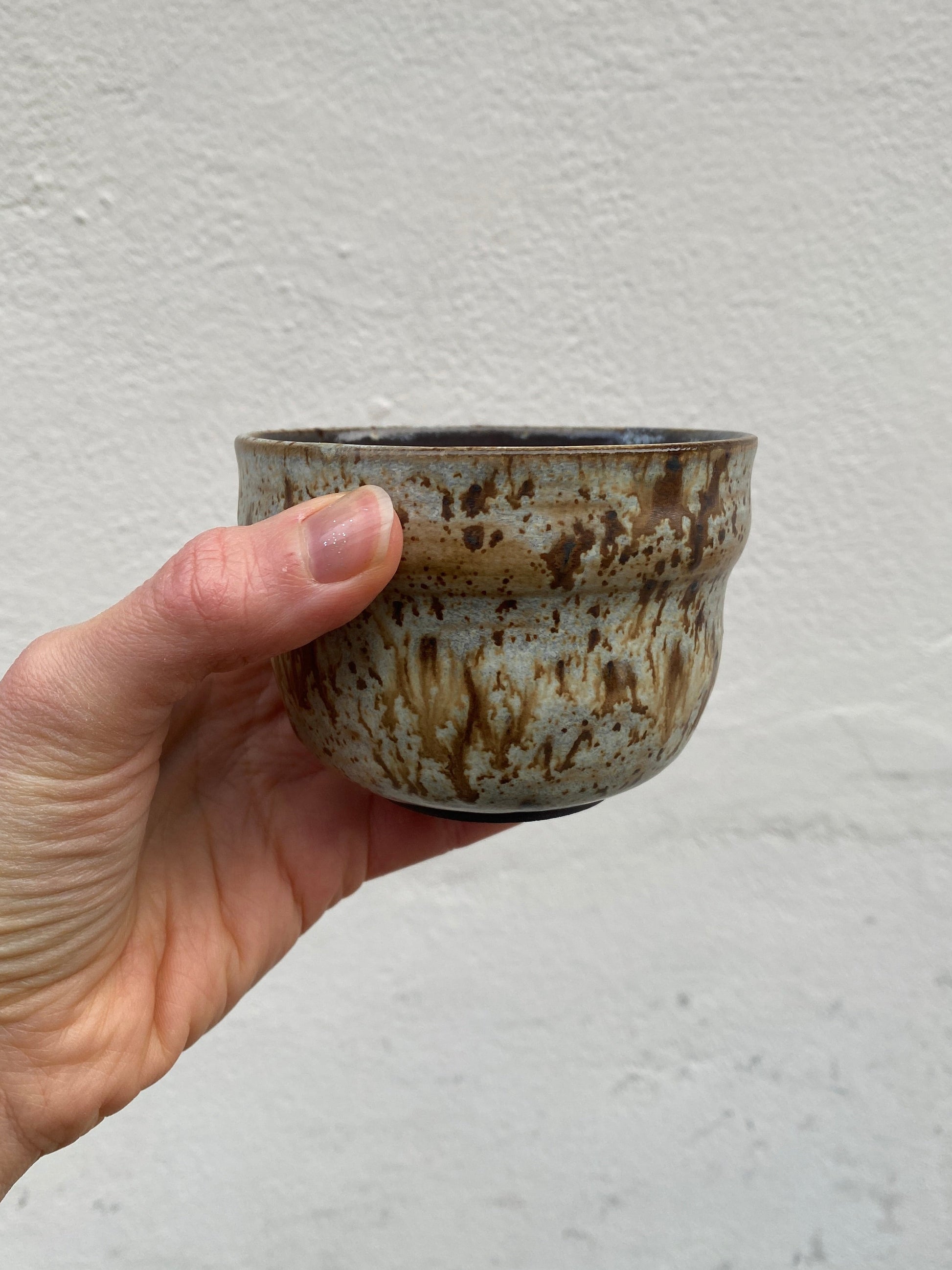 Hand holding a small ceramic cup with a textured surface against a plain background
