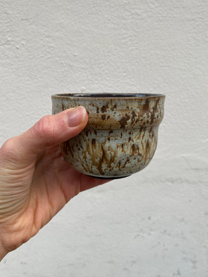 Hand holding a small ceramic cup with a textured surface against a plain background