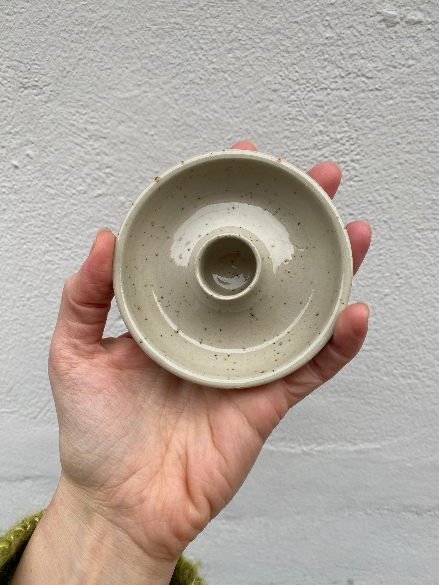 Hand holding a small ceramic candlestick holder against a plain background