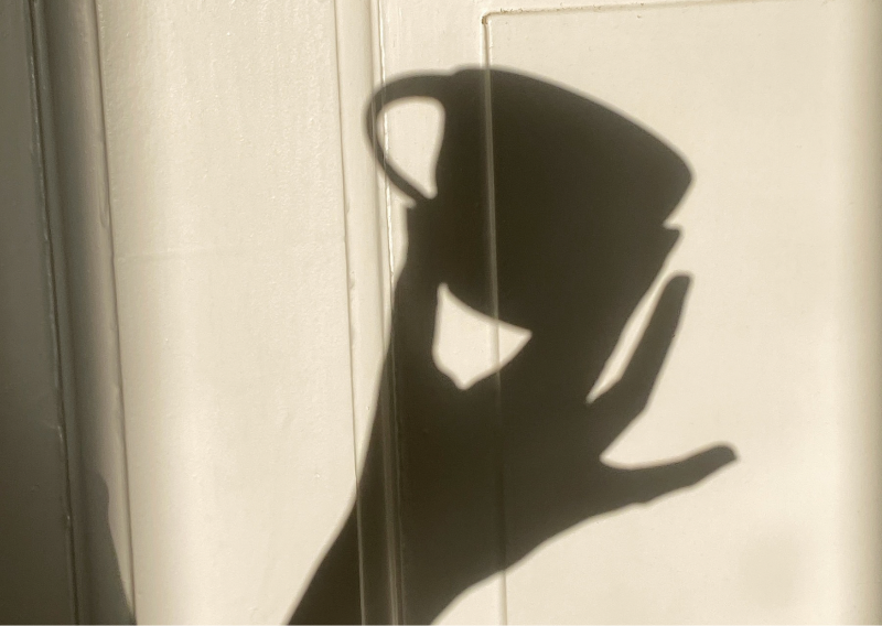 Shadow of a person holding a phone on a light-colored wall